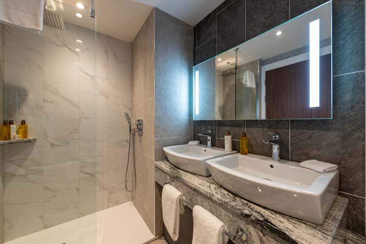 A bathroom with towels, a shower and complimentary toiletries under a large mirror at Ness Walk.