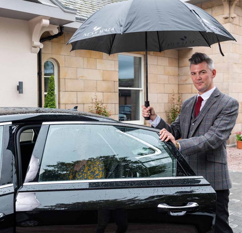 Concierge holding an umbrella sheltering a guest as she exits the car