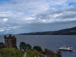 Urquhart Castle with Loch Ness in the background and a Jacobite boat tour passing by.
