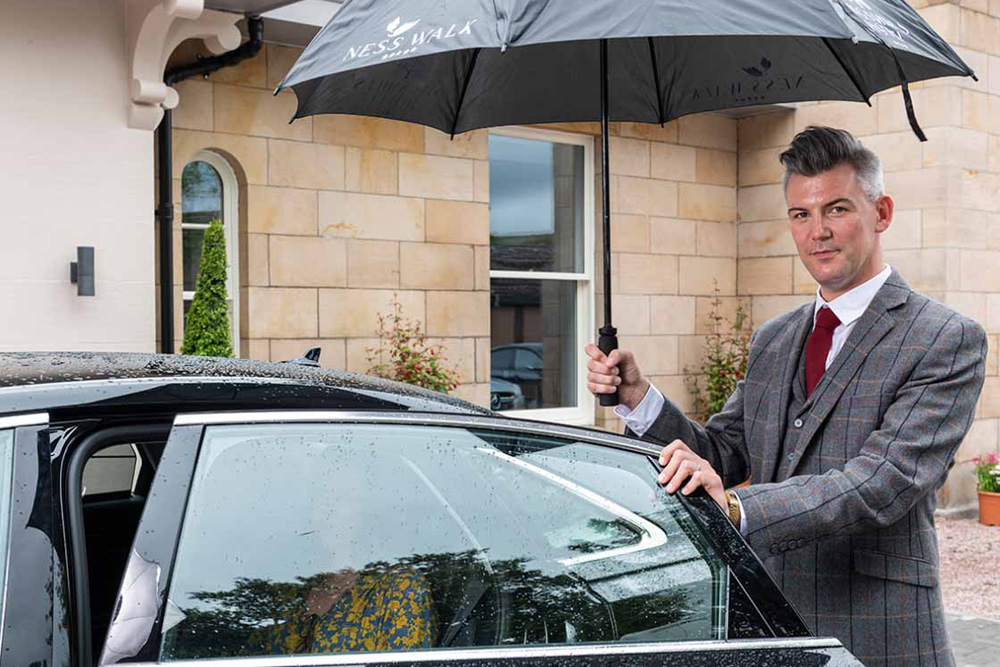 Concierge holding an umbrella sheltering a guest as she exits the car