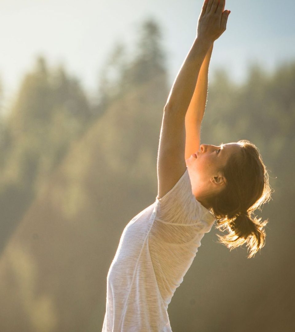 Lady on a lawn doing a yoga pose with hands stretched into the air