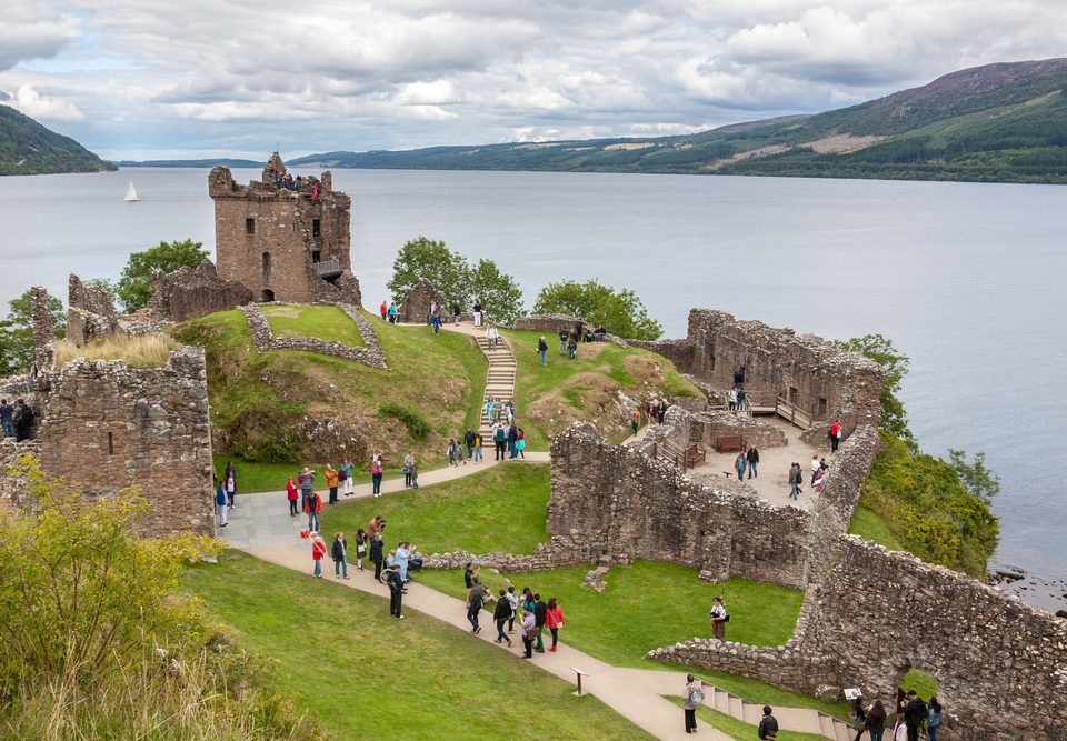 Urquhart Castle with visitors walk around beside Loch Ness in Scotland