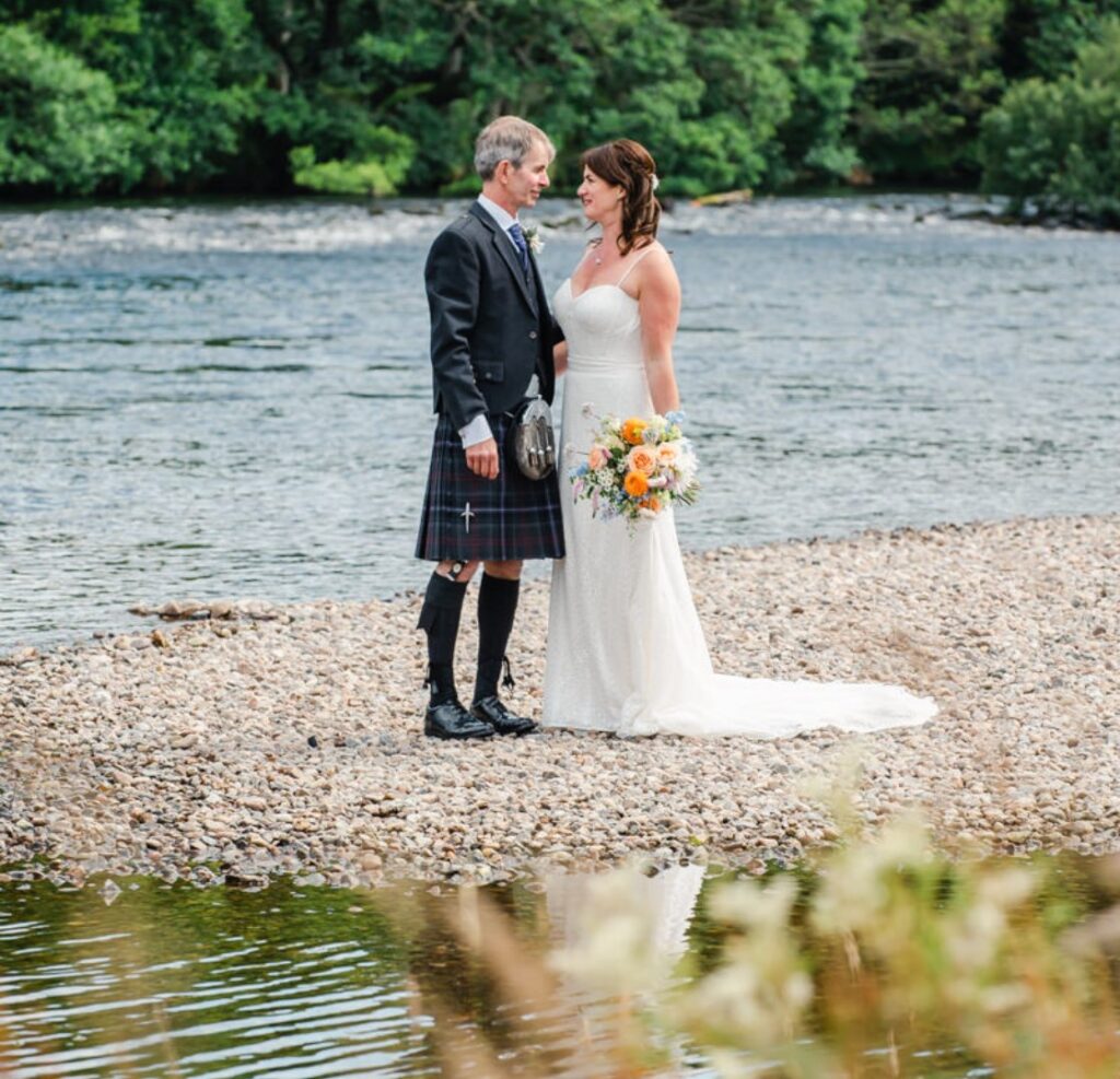 A new bride and groom pose for wedding photos on the banks of River Ness.