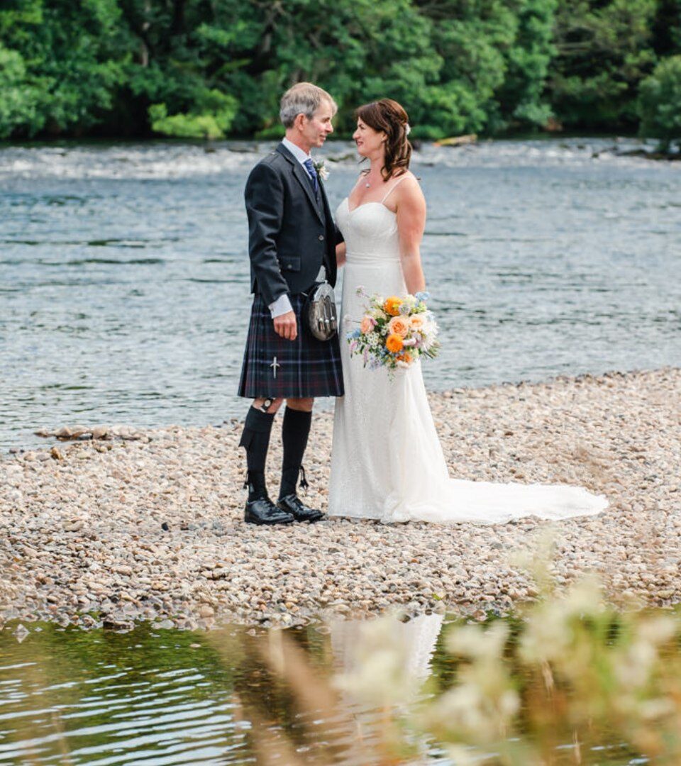 A new bride and groom pose for wedding photos on the banks of River Ness.