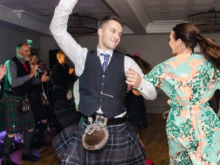 A couple dancing at a Ness Walk Hotel wedding C&egrave;ilidh with guests clapping and wearing kilts.