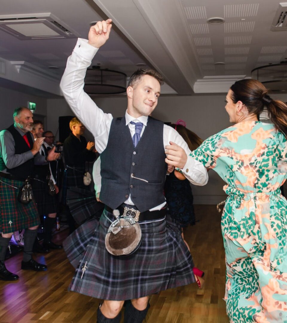 A couple dancing at a Ness Walk Hotel wedding Cèilidh with guests clapping and wearing kilts.