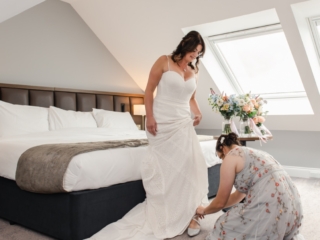 A bridesmaid helps dress the bride in our 5-star luxury bridal suite at Ness Walk Hotel In the Scottish Highlands for her wedding day.