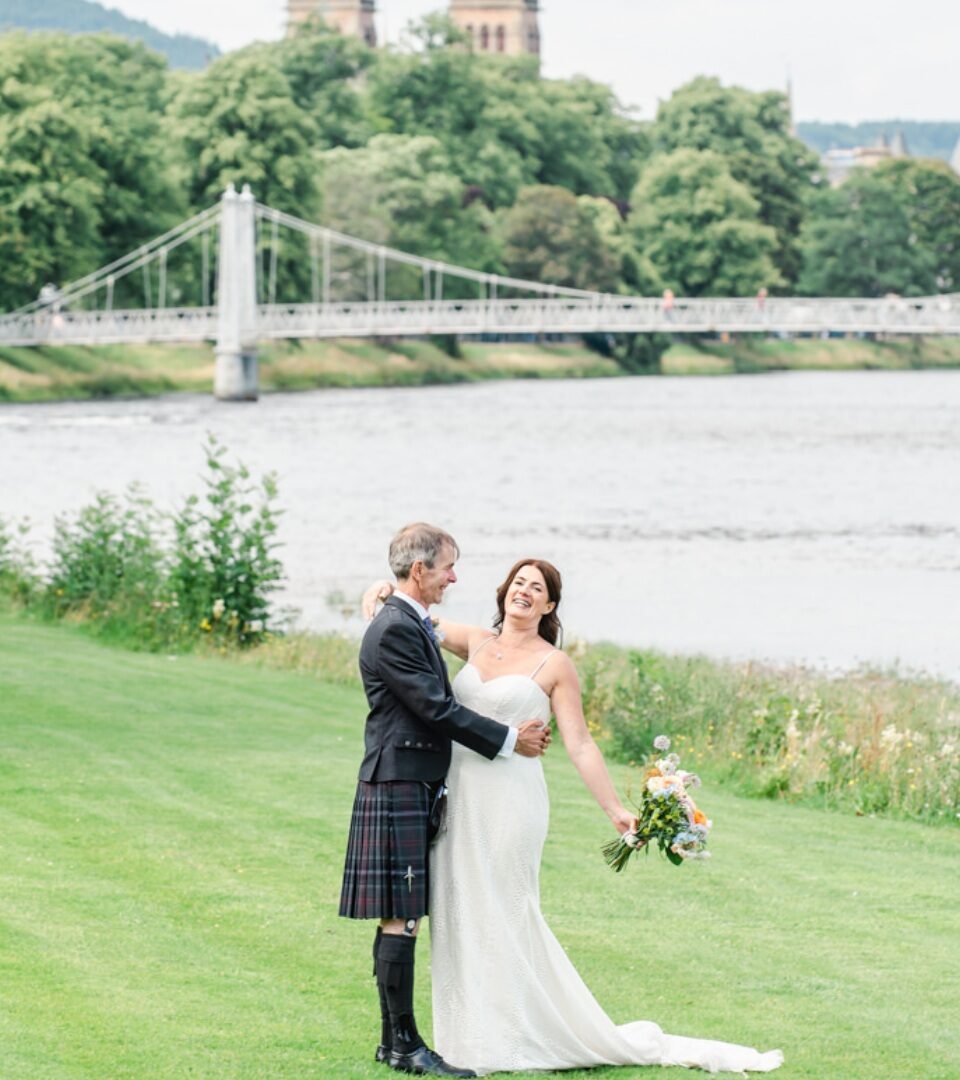 A new bride and groom pose for wedding photos on the banks of River Ness.
