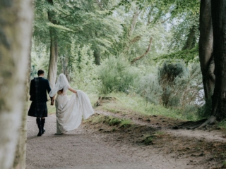 A Scottish wedding photo with a bride and groom walking along the banks of the River Ness with the groom in a kilt.