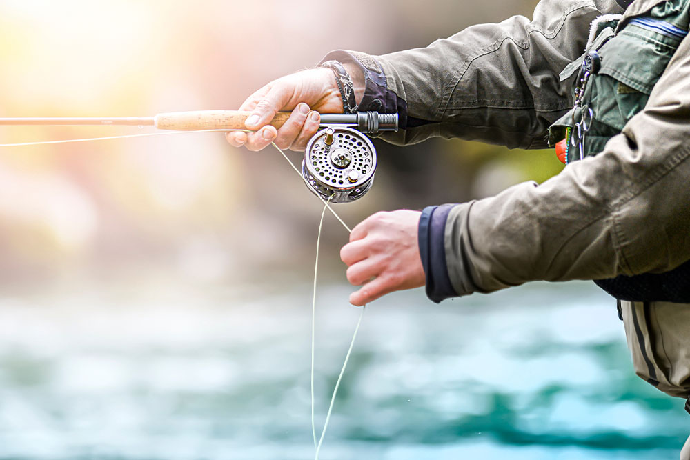 A close up of an angler's hands and rod on a river.