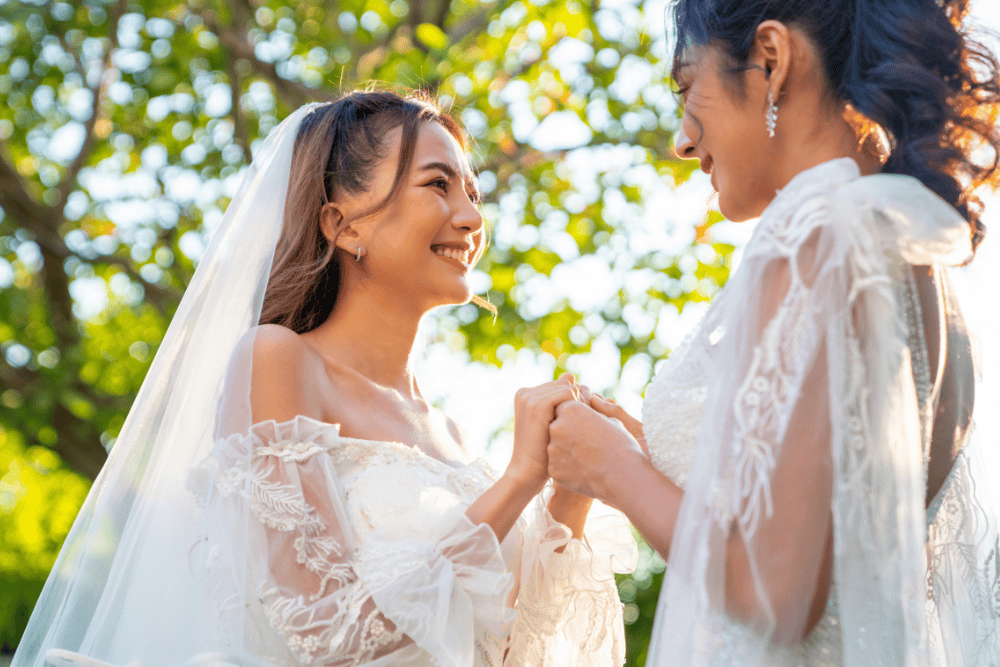 A happy LGBT couple getting married in wedding dresses, holding hands. 