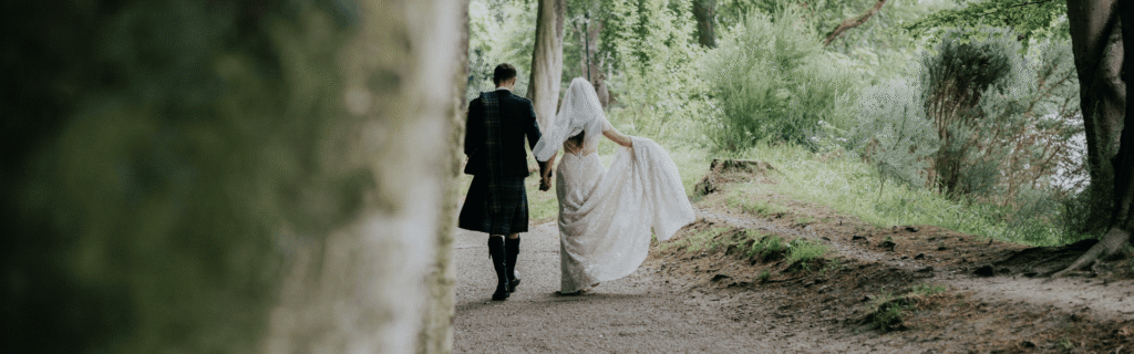 A bride and groom walk hand in hand alongside the River Ness.