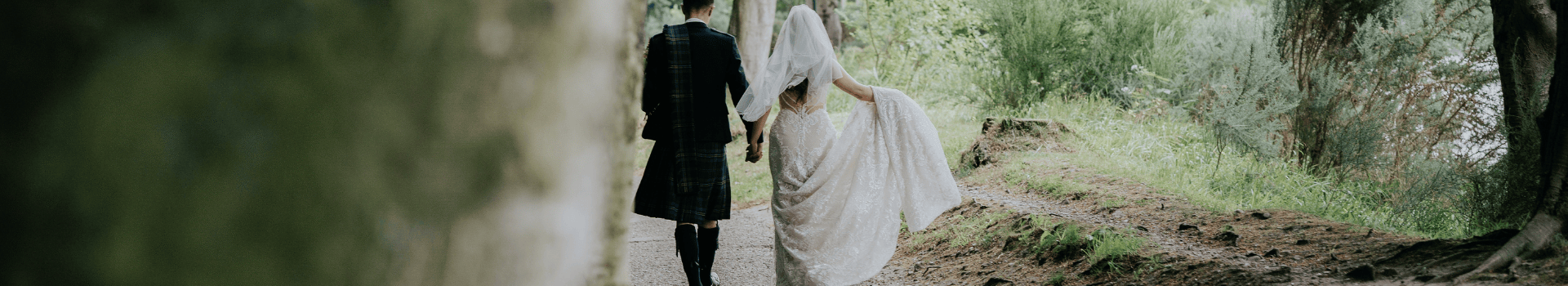 A bride and groom walk hand in hand alongside the River Ness.