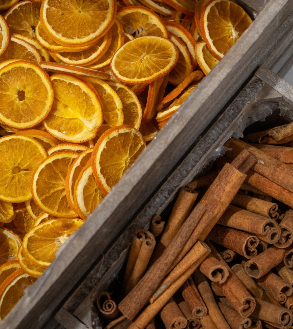 A wooden crate divided into two sections, one filled with dried orange slices and the other with cinnamon sticks, used as natural decorative elements in the festive arrangement workshop