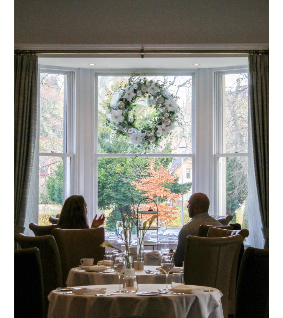Two guests in front of a bay window with a snowcapped Christmas wreath hanging between them. Sat in Torrish restaurant.