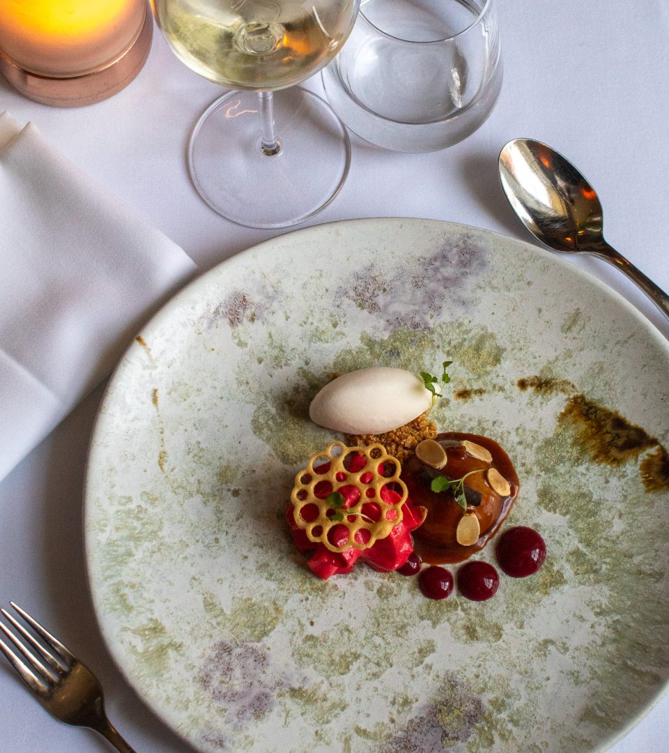 A beautifully plated festive dessert served during Christmas Day lunch at Ness Walk, accompanied by white wine, elegant tableware and a candlelit fine dining setting.