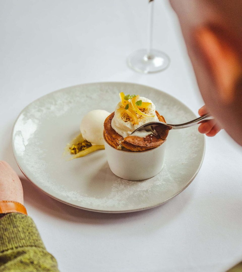 A beautifully presented Christmas Day Lunch dessert at Ness Walk, featuring a light soufflé topped with toasted cream and citrus garnish, served with a scoop of vanilla ice cream and pistachio crumble on an elegant white plate.