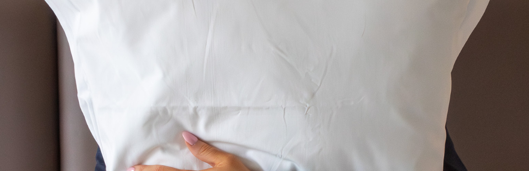 Guest in navy pyjamas hugging a plump white pillow while sitting up in bed at Ness Walk